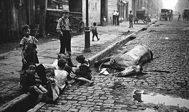 Children play in the gutters next to a horse carcass in this powerful photo taken in New York City, NY, in 1900.  The gutters and the cobblestone street surface are separated by a collection channel, shown at the children’s feet, for collecting and conveying dirt, debris, stormwater, and other cast off waste in lieu of a municipal sanitation system at this point in history. Photo Source: Ephemeral New York 